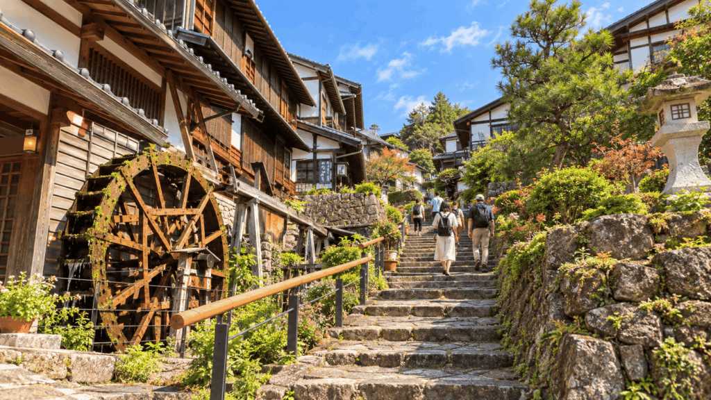 Visitors walking past traditional houses and a waterwheel in Magome-juku