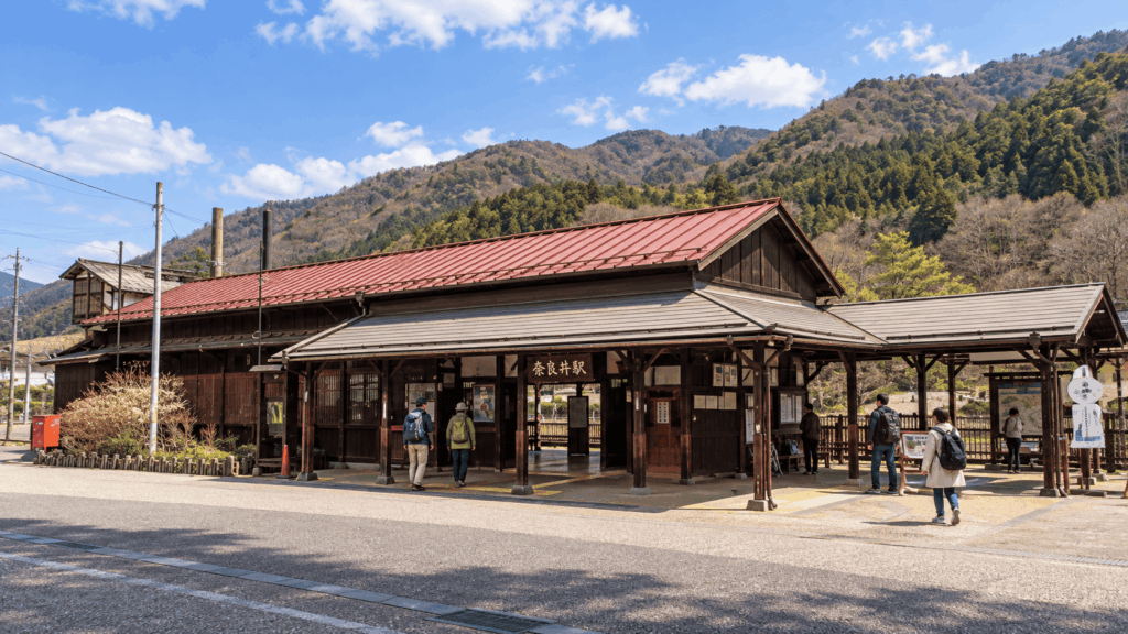 Travelers outside the traditional wooden Narai Station surrounded by mountains in spring