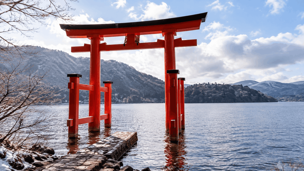 Red torii gate of Hakone Shrine standing in Lake Ashi with snow-covered mountains in the background