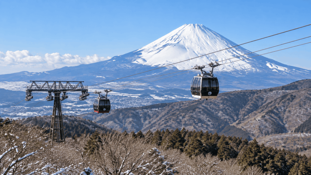Hakone Ropeway cable cars traveling above snowy mountains with a panoramic view of snow-capped Mount Fuji