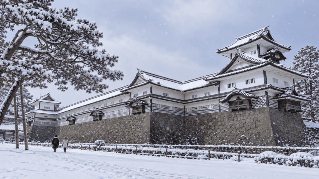 Historic white walls and tiled roofs of Kanazawa Castle covered in snow during a winter snowfall