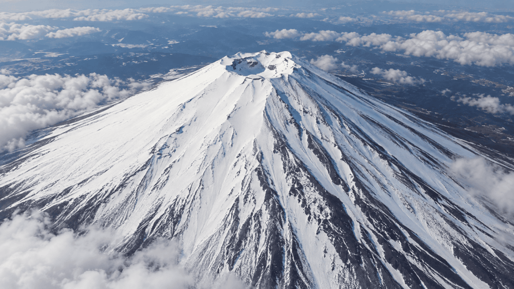 Aerial view of Mount Fuji's snow-covered summit and volcanic crater surrounded by clouds in winter