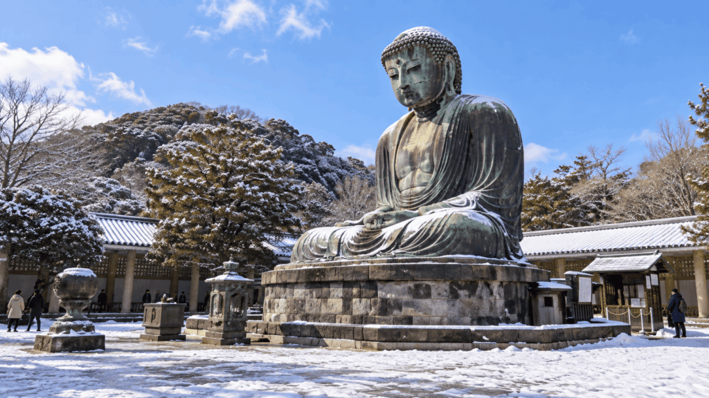 Great Buddha of Kamakura at Kotokuin Temple surrounded by snow-covered trees under a clear winter sky