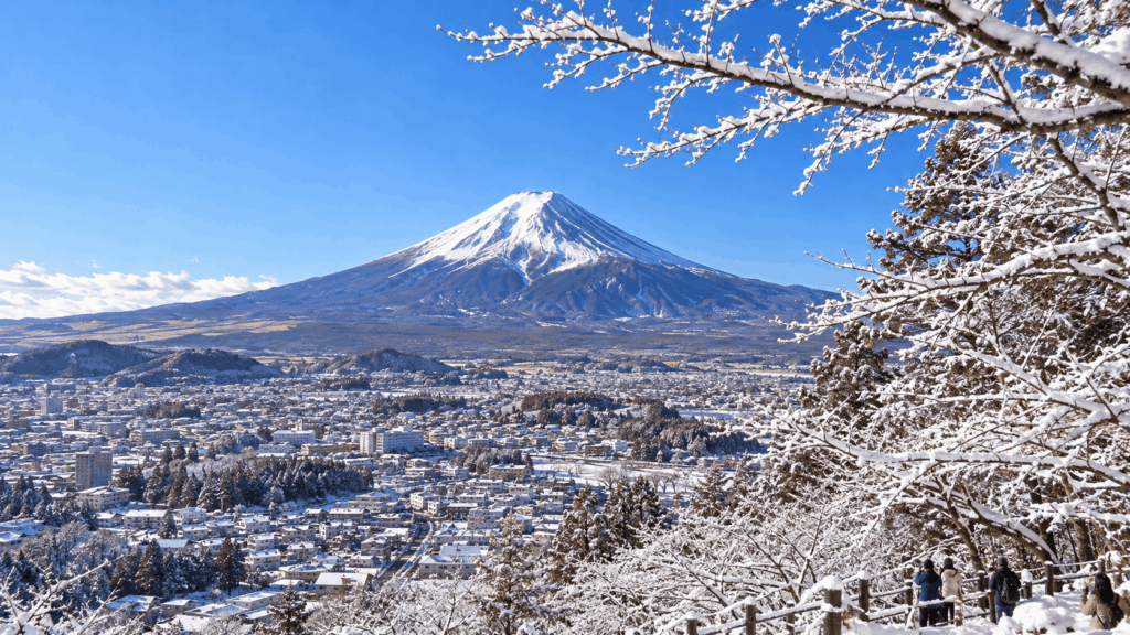 Snow-covered Mount Fuji rising above a winter landscape with snowy trees and town buildings in Japan