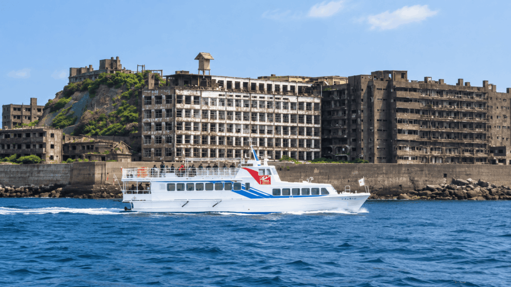 White passenger ferry cruising past abandoned coal mining apartment buildings on Ikeshima Island, Nagasaki