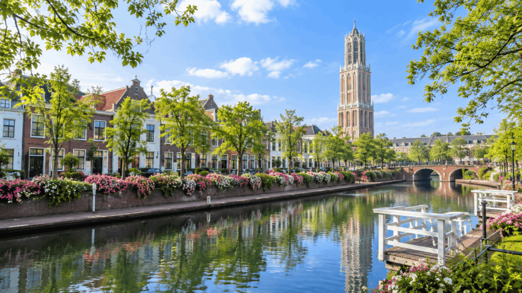 Scenic canal lined with colorful flowers and Dutch-style buildings beneath the Domtoren tower at Huis Ten Bosch, Nagasaki