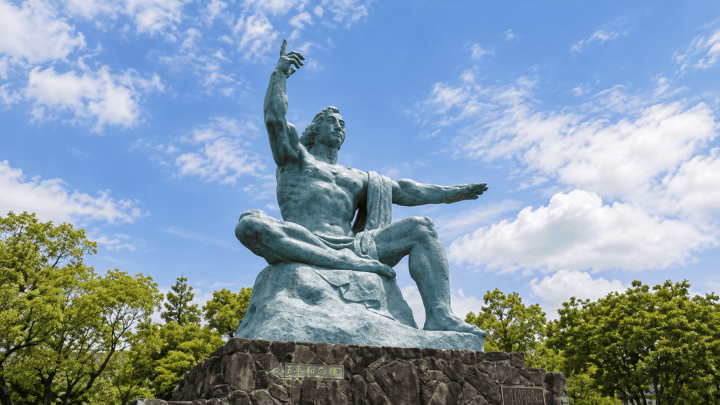 Nagasaki Peace Statue in Peace Park, showing a seated figure pointing toward the sky beneath a bright blue sky