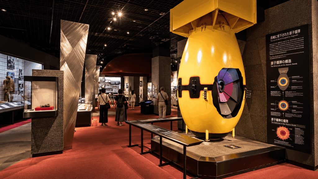 Interior exhibition at the Nagasaki Atomic Bomb Museum, featuring a yellow atomic bomb model, historical displays, and visitors