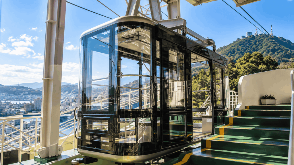 Glass cabin of the Nagasaki Ropeway at a hillside station, with panoramic views of the city and Mount Inasa in the background