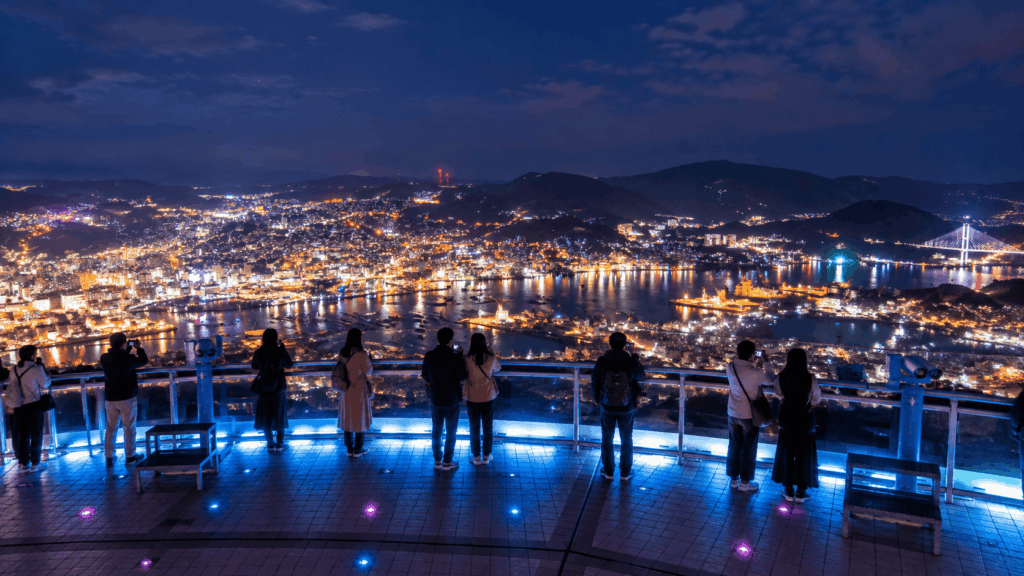 Tourists enjoying the panoramic night view of Nagasaki city and harbor from the illuminated Mount Inasa observation deck