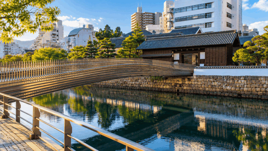 Pedestrian bridge crossing the water toward restored traditional buildings at Dejima, Nagasaki, with reflections in the canal