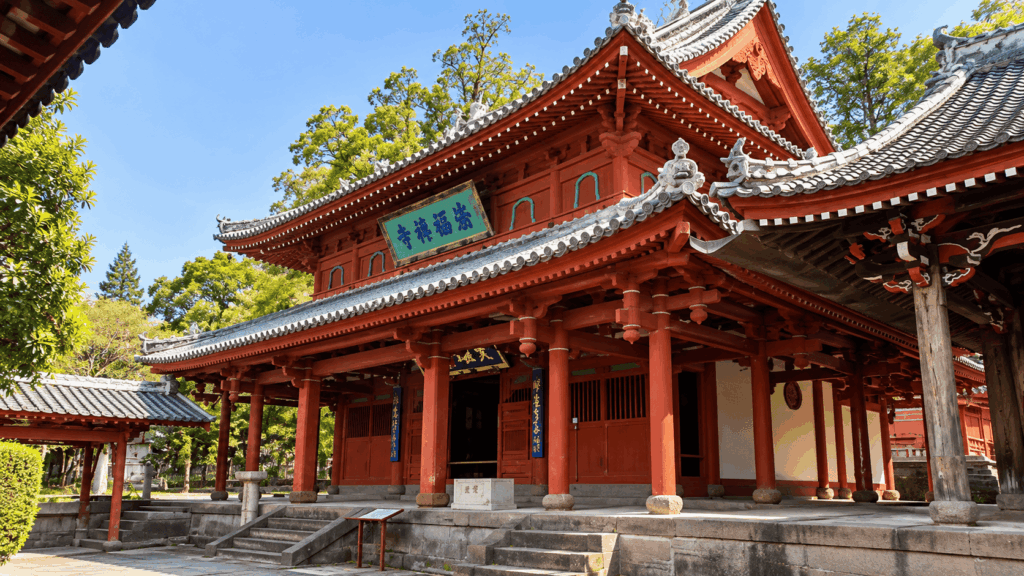 Traditional red wooden architecture and ornate tiled roofs of Sofukuji Temple in Nagasaki beneath a clear blue sky